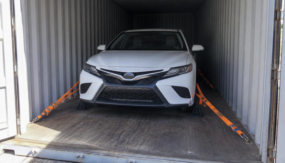 White sedan secured with straps inside a shipping container